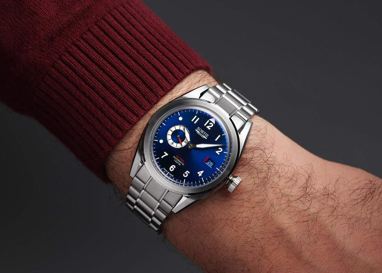 Silver stainless steel watch with a blue dial, white numerals and red colour accents. Includes a seconds hand dial and date display. Shown on a person's wrist.